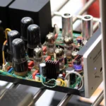 Car audio technician checking amp grounding with a multimeter in a garage