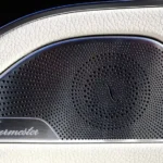 Component speakers and coaxial speakers laid out on a garage workbench beside an open car door.