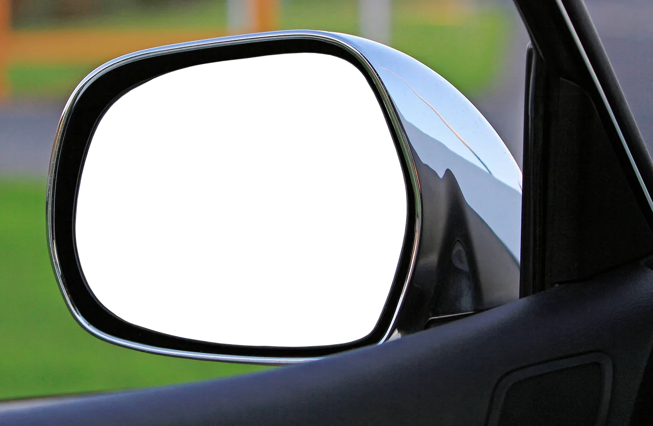 Driver compares a rearview mirror monitor and wiring options beside an open car door.