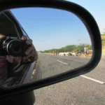 A driver checks a rear dash cam display in a parked car at dusk