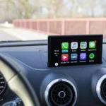 Driver using wireless CarPlay in a car interior with a phone on the dashboard near the stereo
